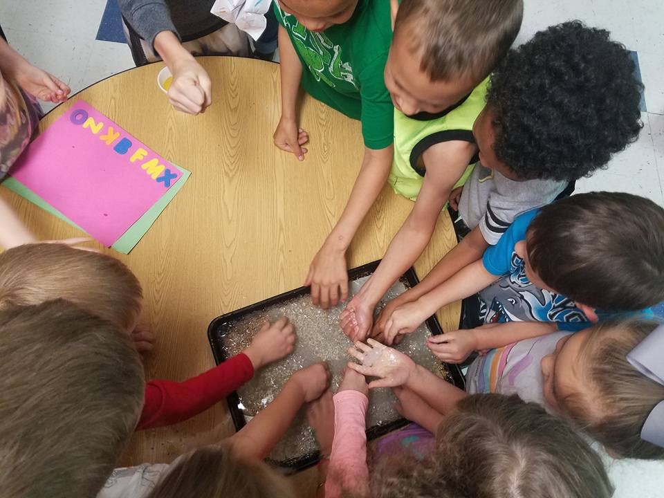 Children gathered around a table with their hands in a sensory bin