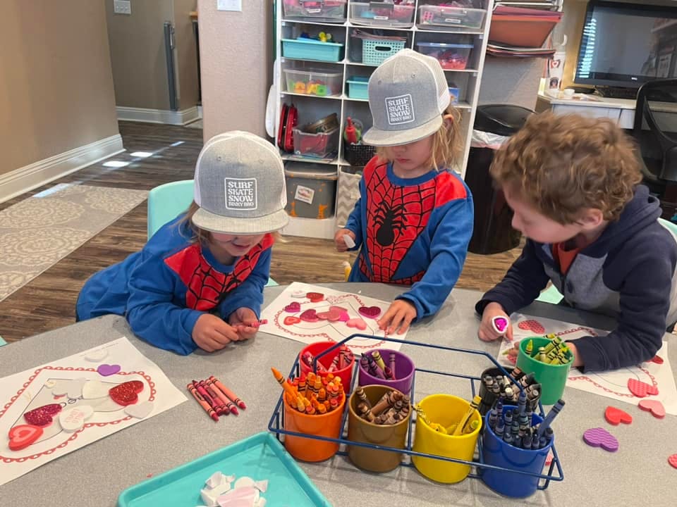 Three children at a table coloring and crafting with paper hearts
