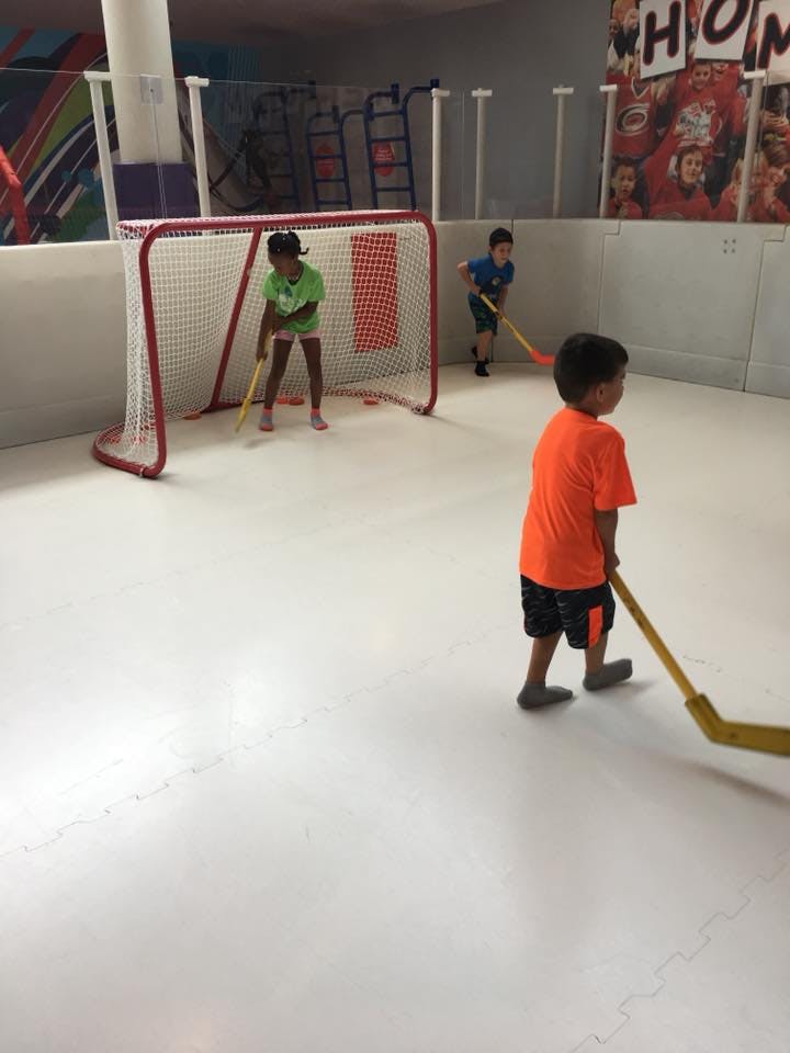 Three children playing floor hockey with sticks and a goal