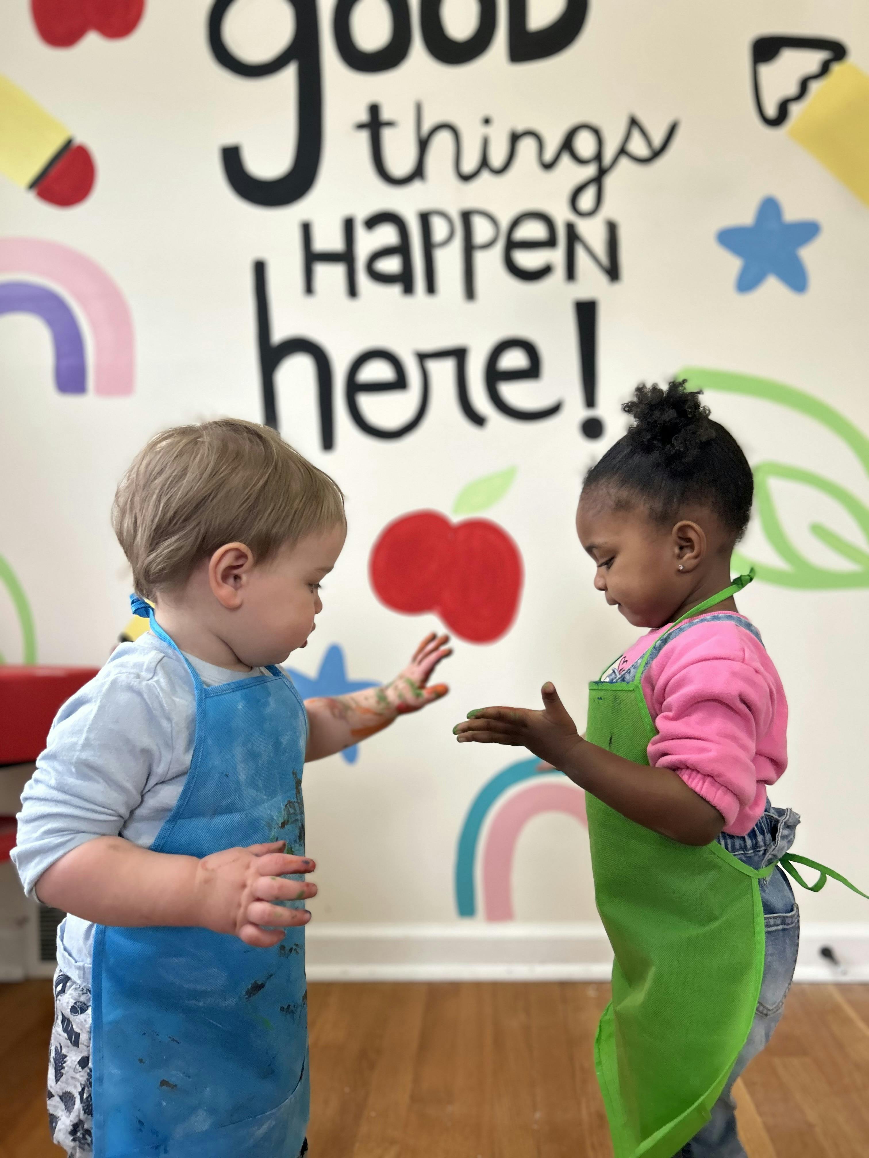 Two children wearing aprons, with paint on their hands