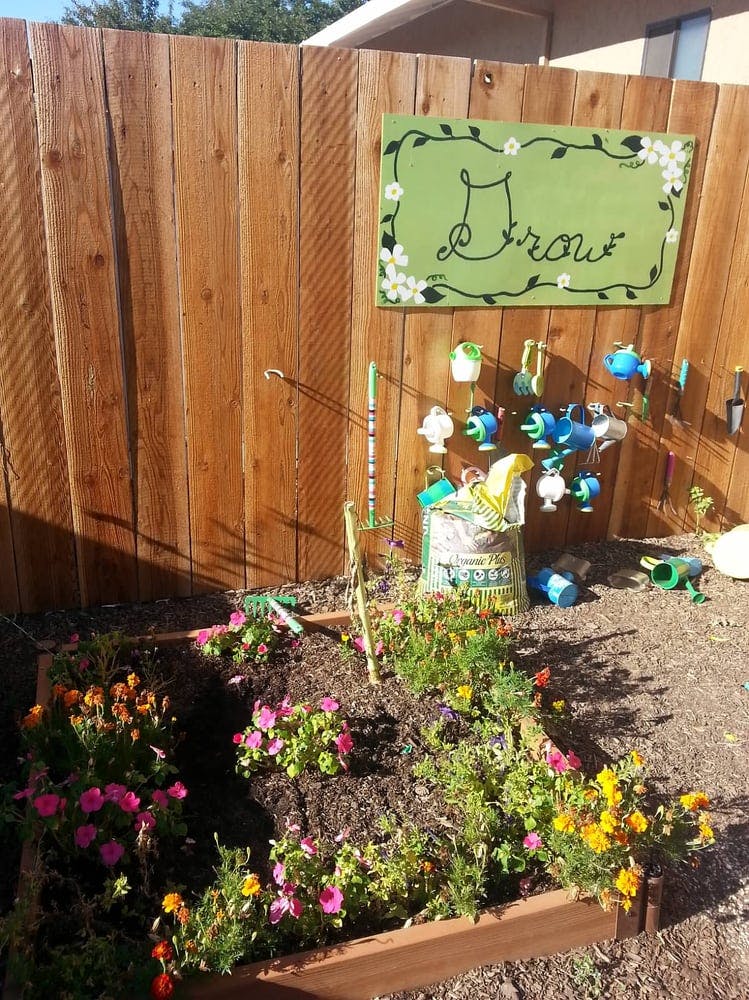 Raised garden bed with flowers and gardening tools hanging on a fence