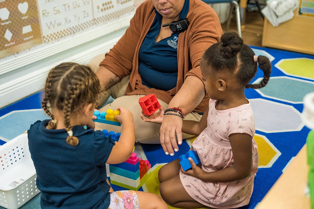 Adult and two children playing with blocks on a rug