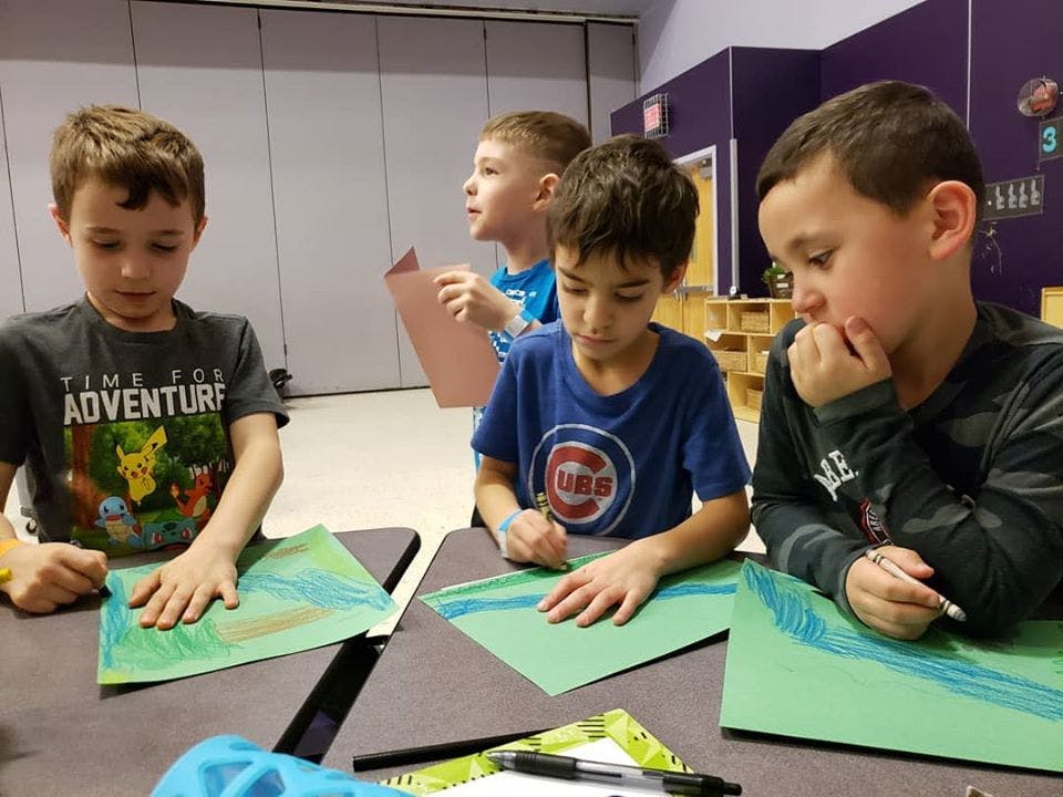 Three children drawing on green paper at a table