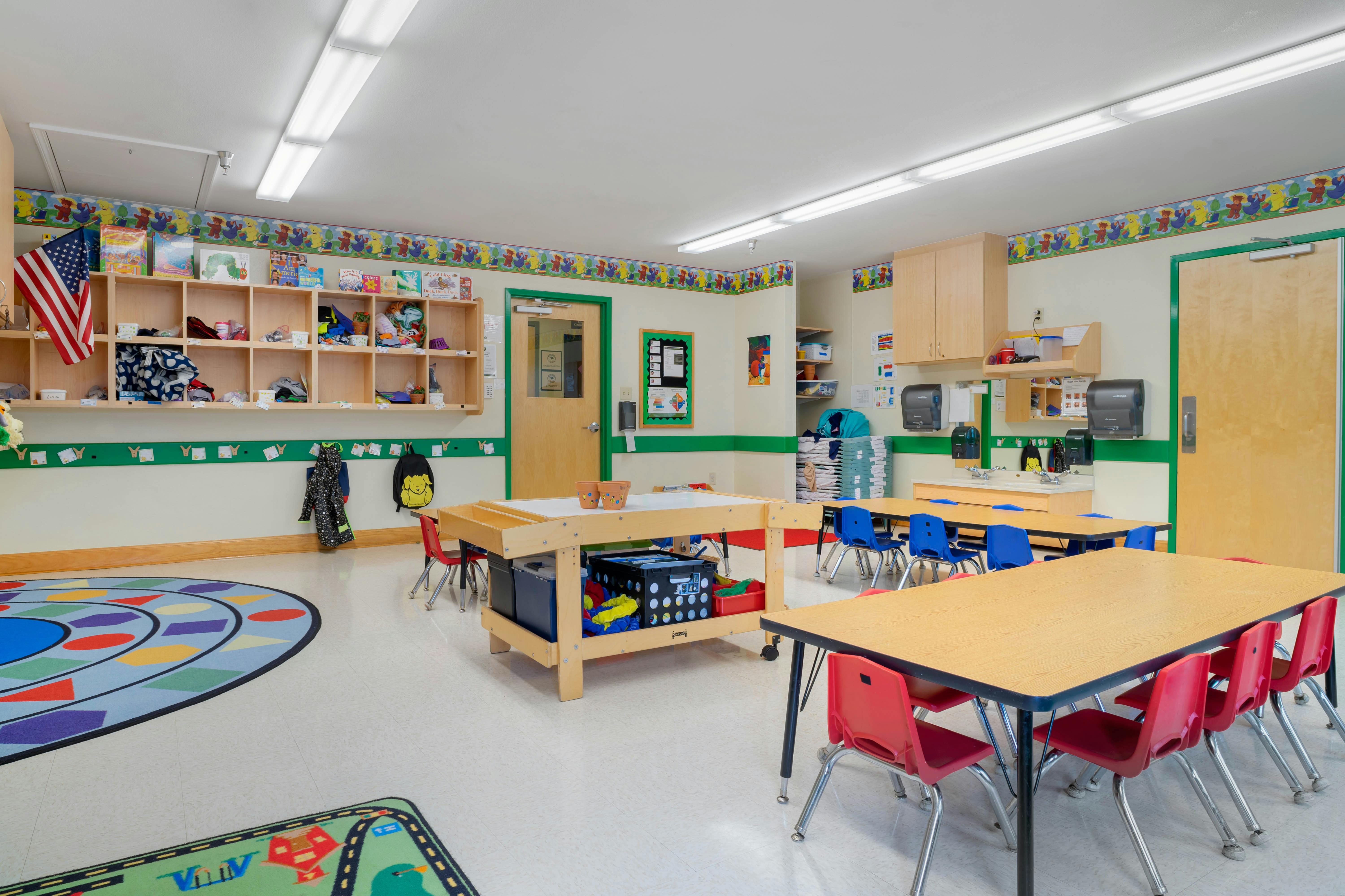 Classroom with tables, chairs, shelving units, and colorful rugs