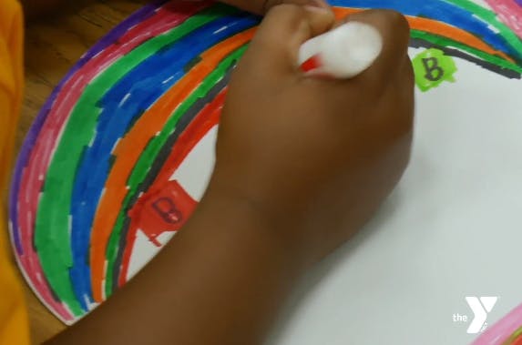 Child's hand coloring a paper plate with a marker