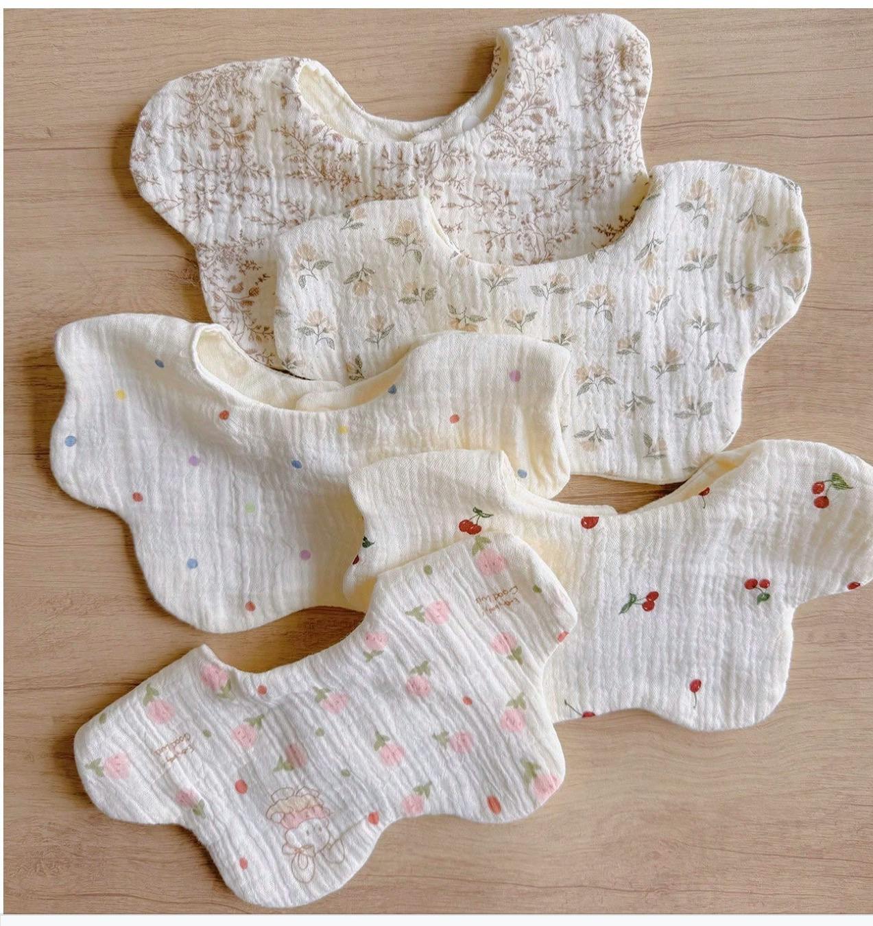 Five baby bibs with various patterns like flowers, polka dots, and cherries