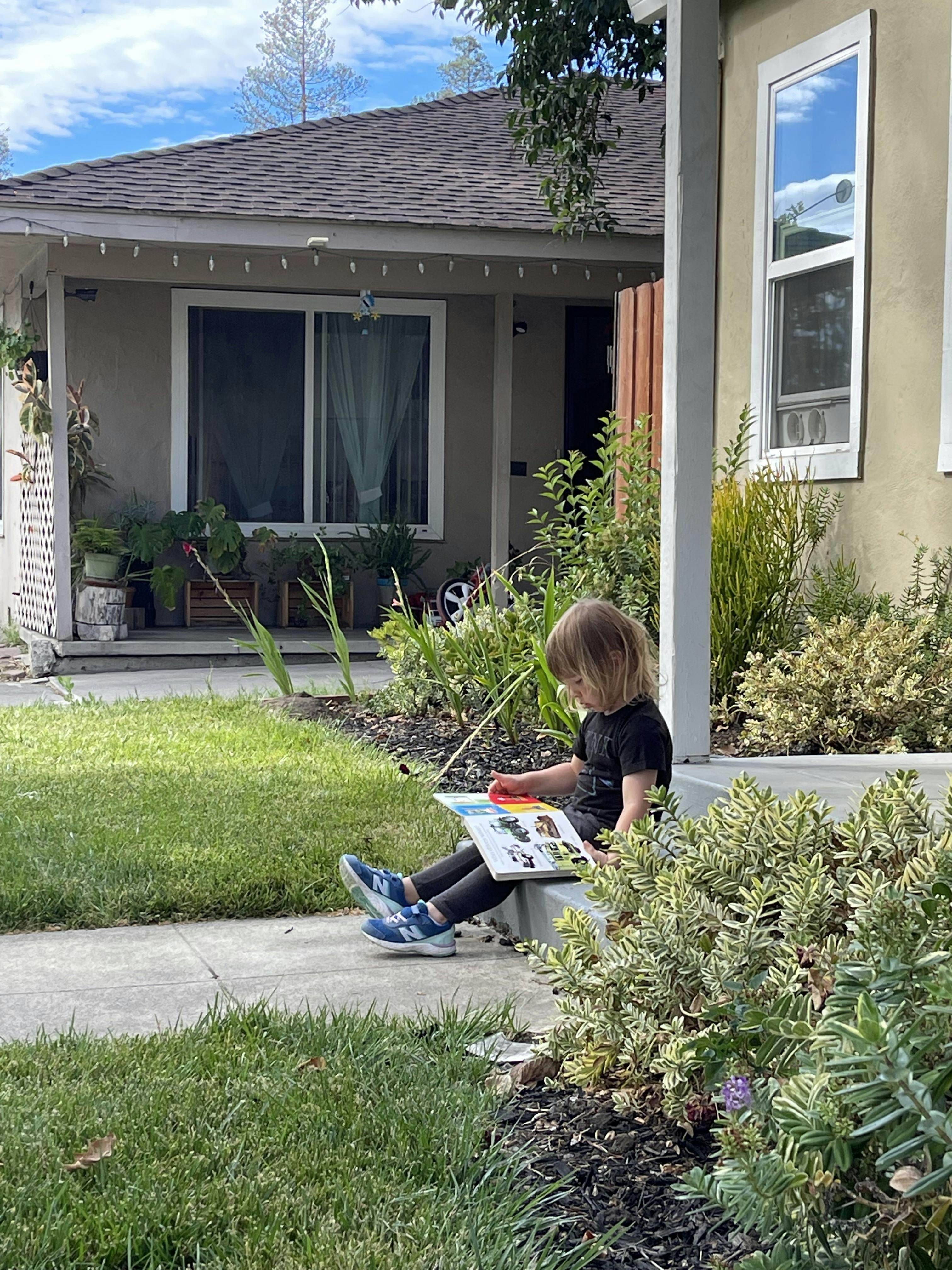 Child sitting on a step and reading a book outdoors