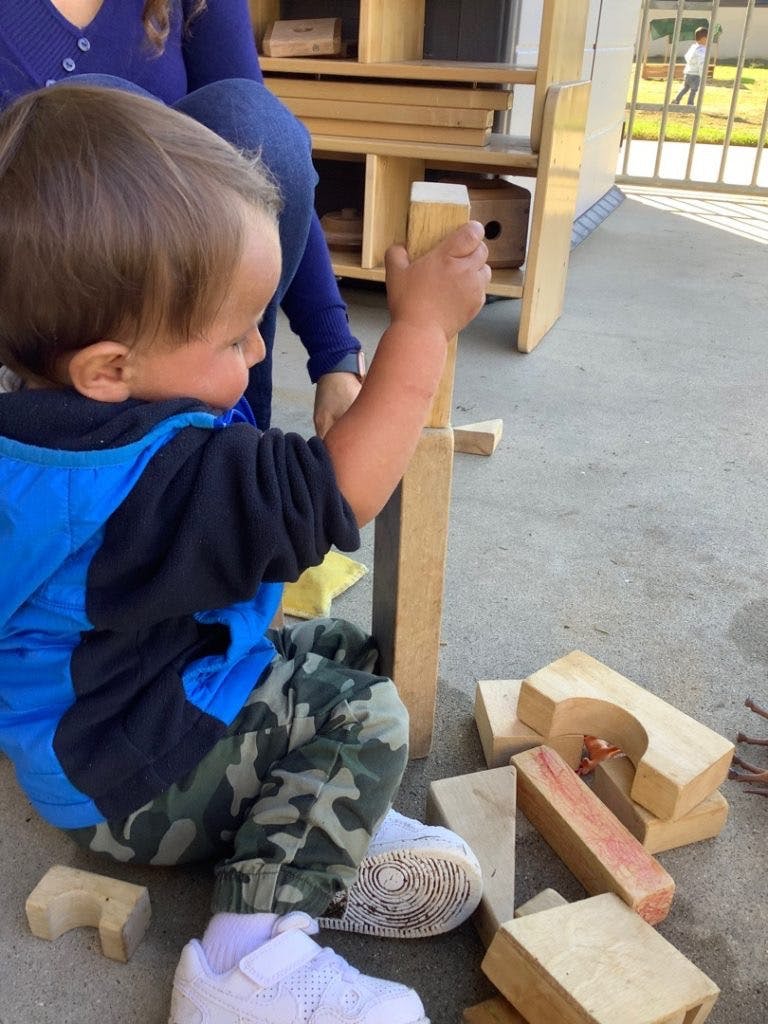 Child in blue jacket playing with wooden blocks on the ground