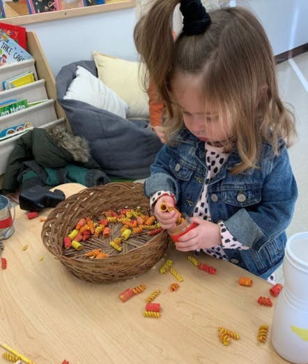 Child playing with colorful pasta pieces on a table