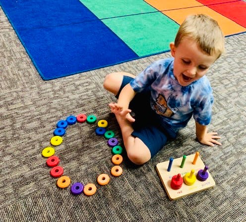 Child playing with colorful rings and a pegboard toy on a carpeted floor