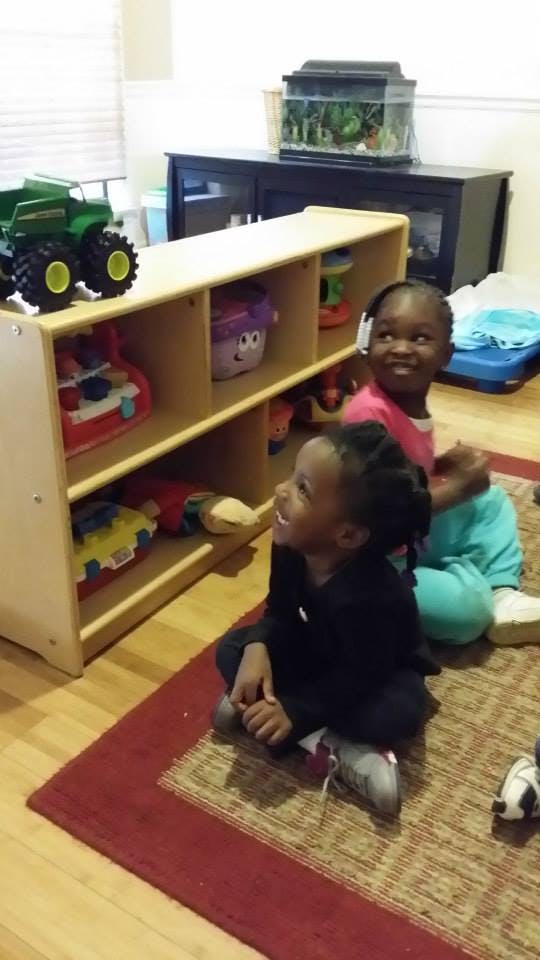 Two children sitting on a rug next to a toy shelf