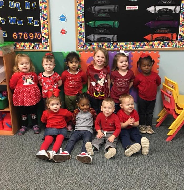 Group of young children in red shirts standing and sitting in a classroom