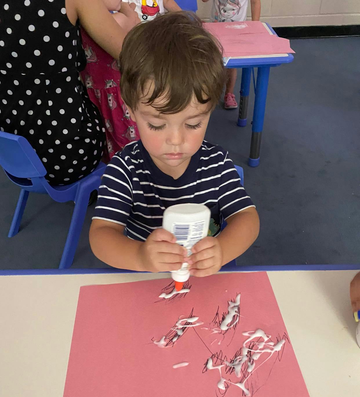 Child squeezing glue onto red paper