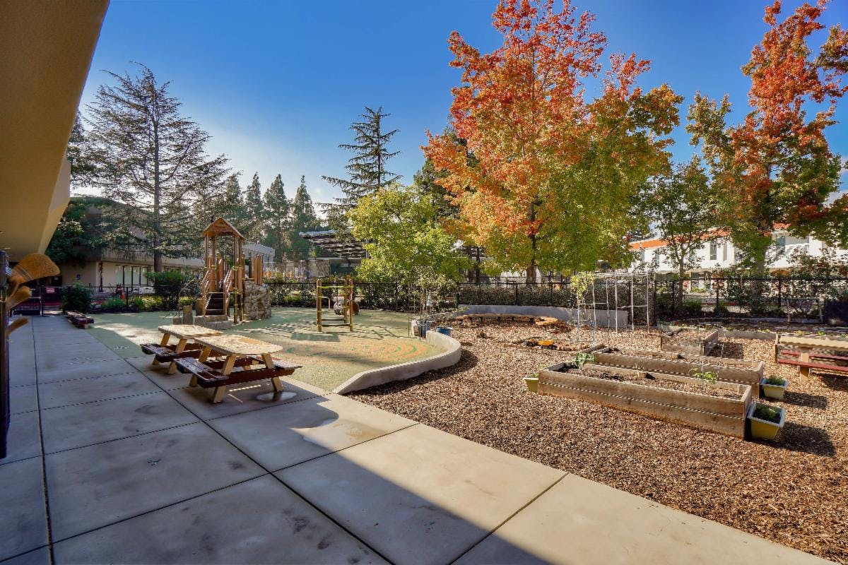 Outdoor playground with picnic tables, play structures, and raised garden beds
