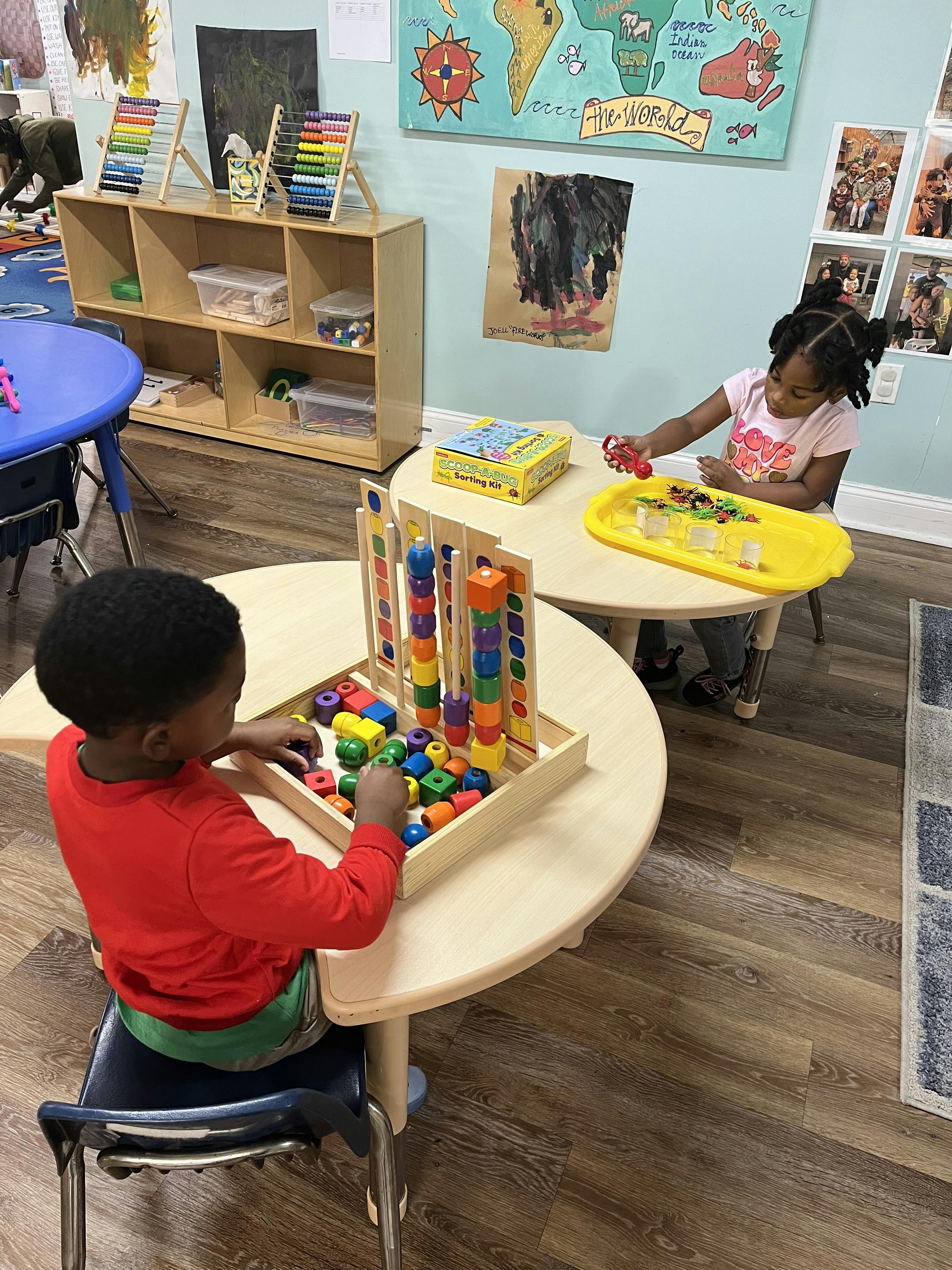 Child playing with a sorting kit, child at another table building with blocks
