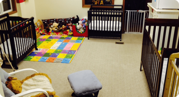 Three cribs in a room with a colorful playmat