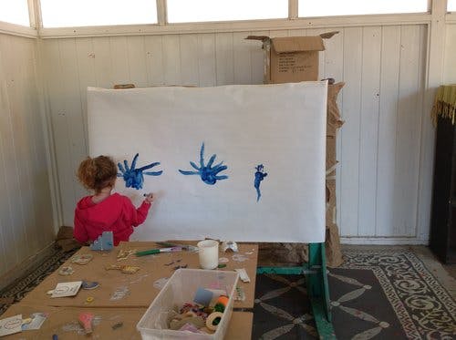 Child painting blue shapes on a large white canvas