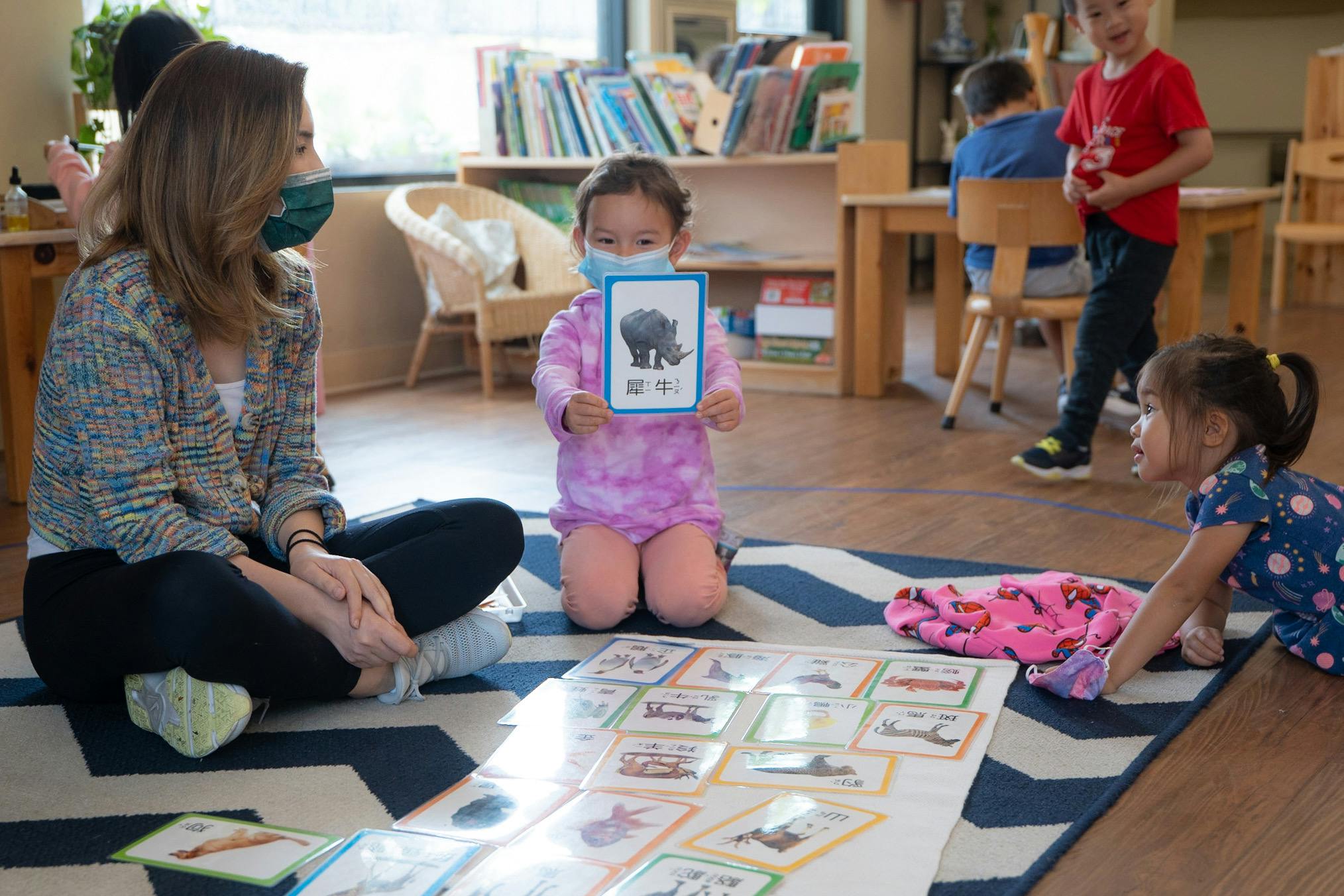 Adult and child on floor, child holding up a card with a rhinoceros