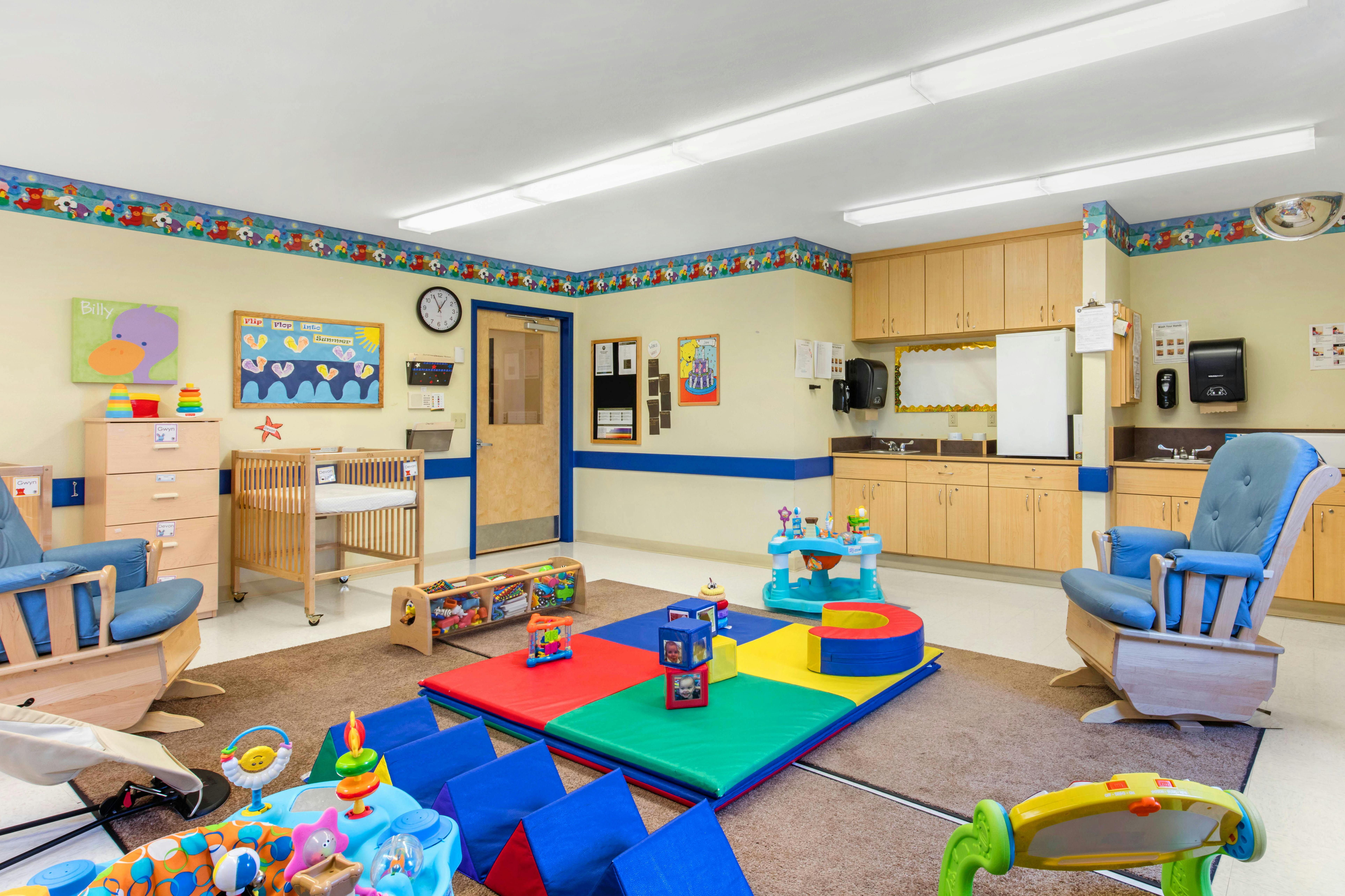 Childcare room with cribs, rocking chairs, play mats, and toys