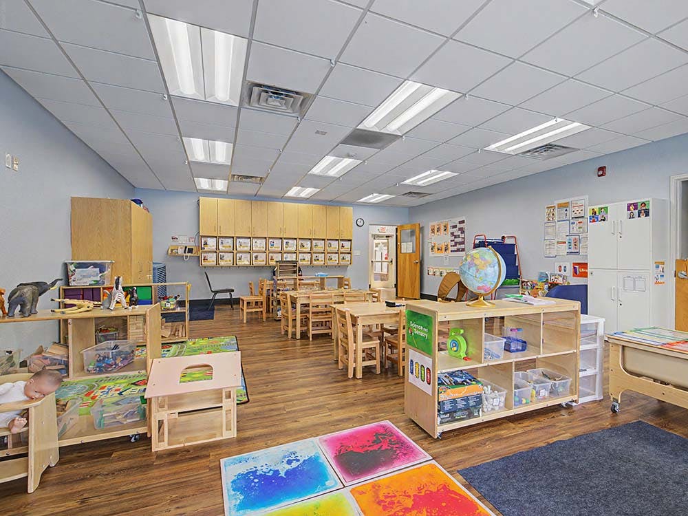 Classroom with small wooden tables and chairs, toys, and cabinets