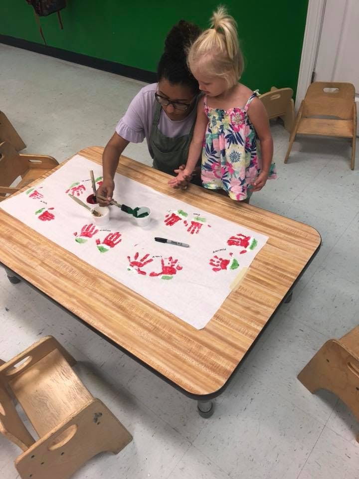 Person and child painting handprints on paper at a table