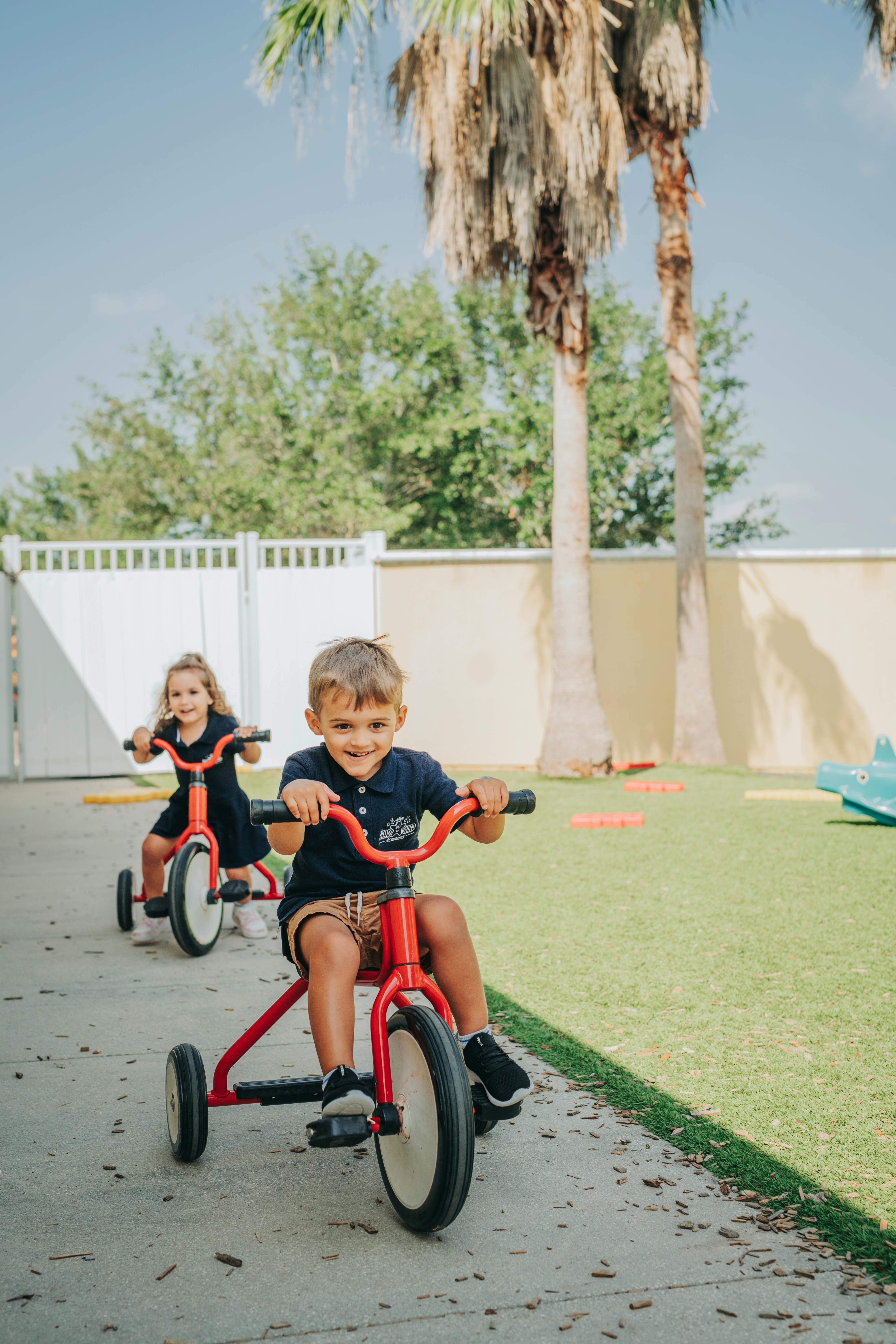 Two children riding red tricycles outdoors