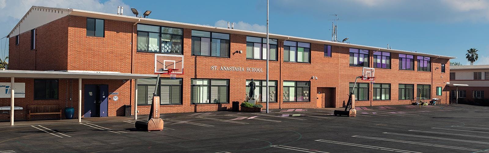 Exterior of St. Anastasia School with basketball hoops on a paved court