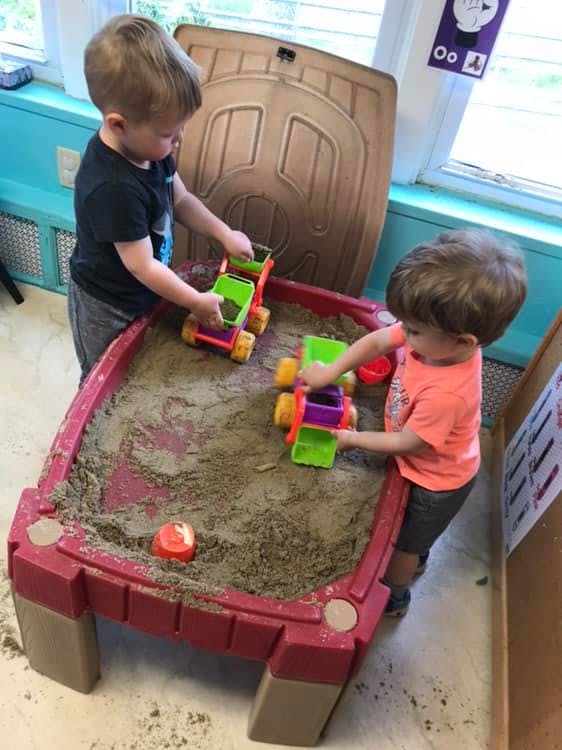 Two children playing with toy trucks in a sandbox