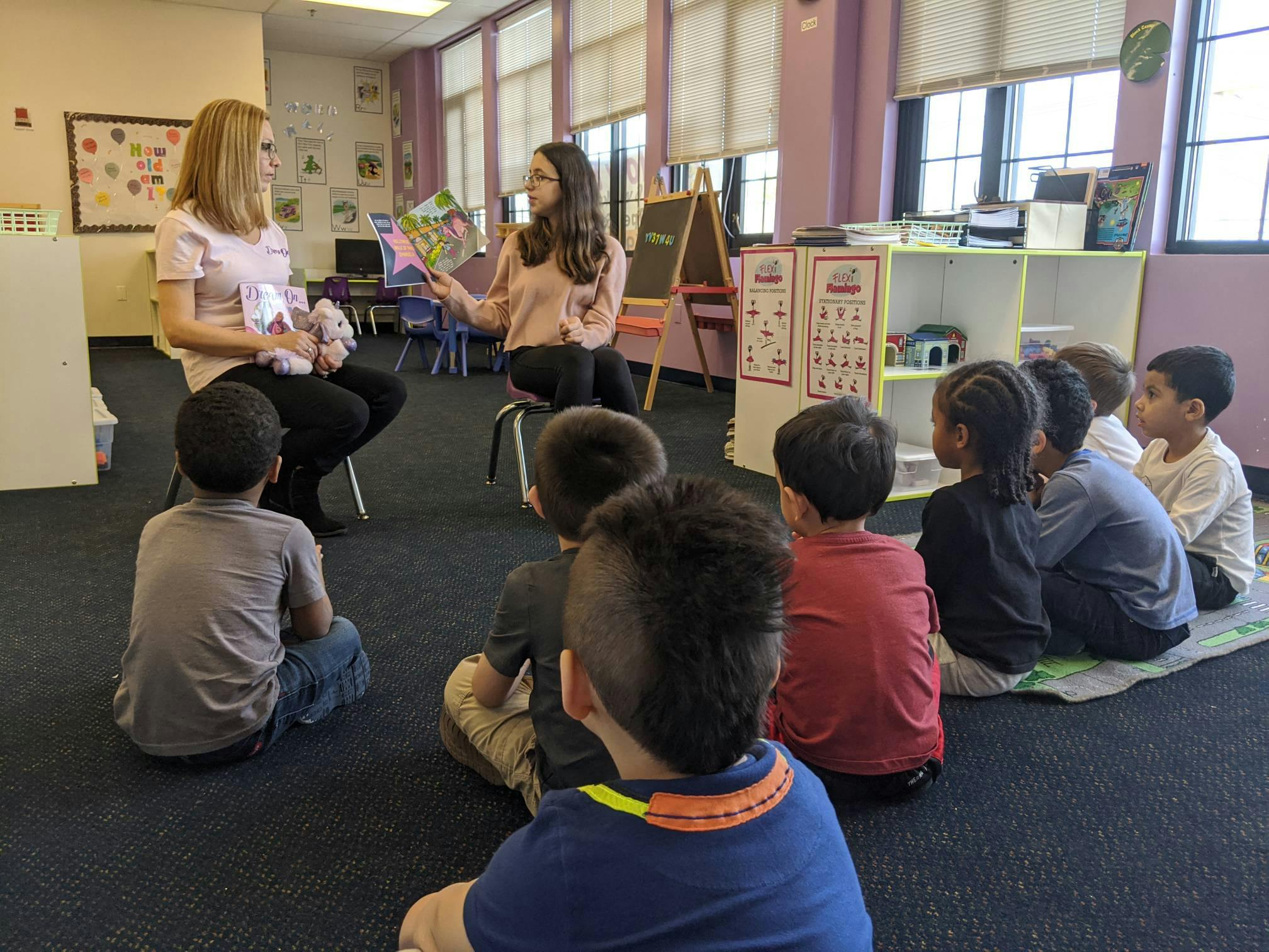 Two people reading to a group of children in a classroom