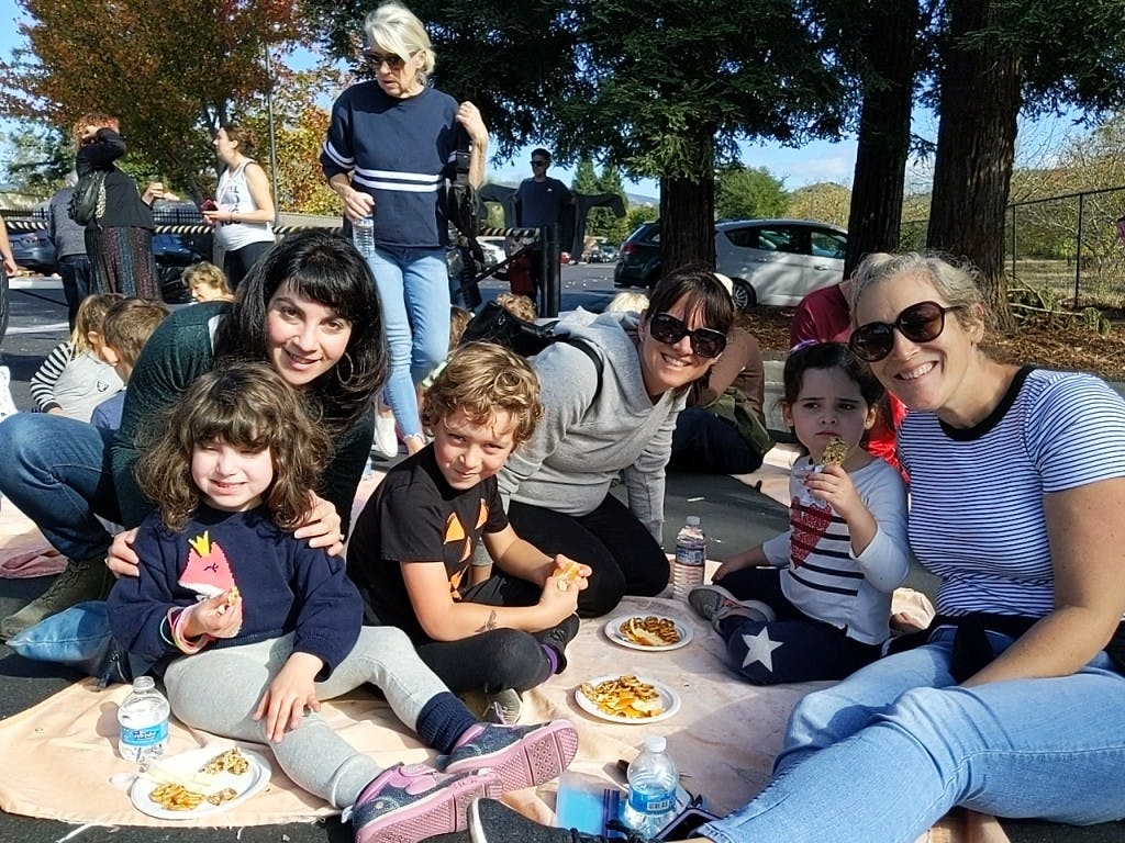 People and children sitting on a blanket outdoors with food