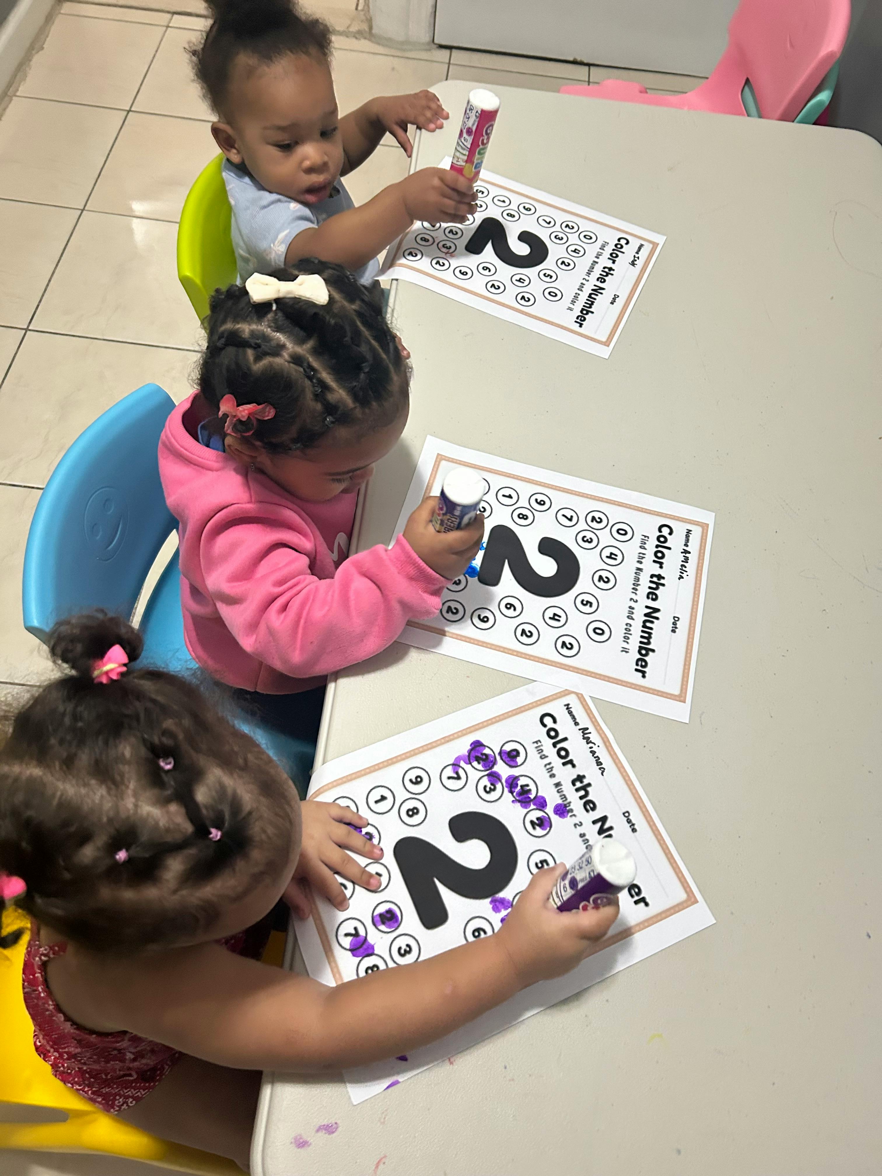 Three children coloring number 2 worksheets at a table