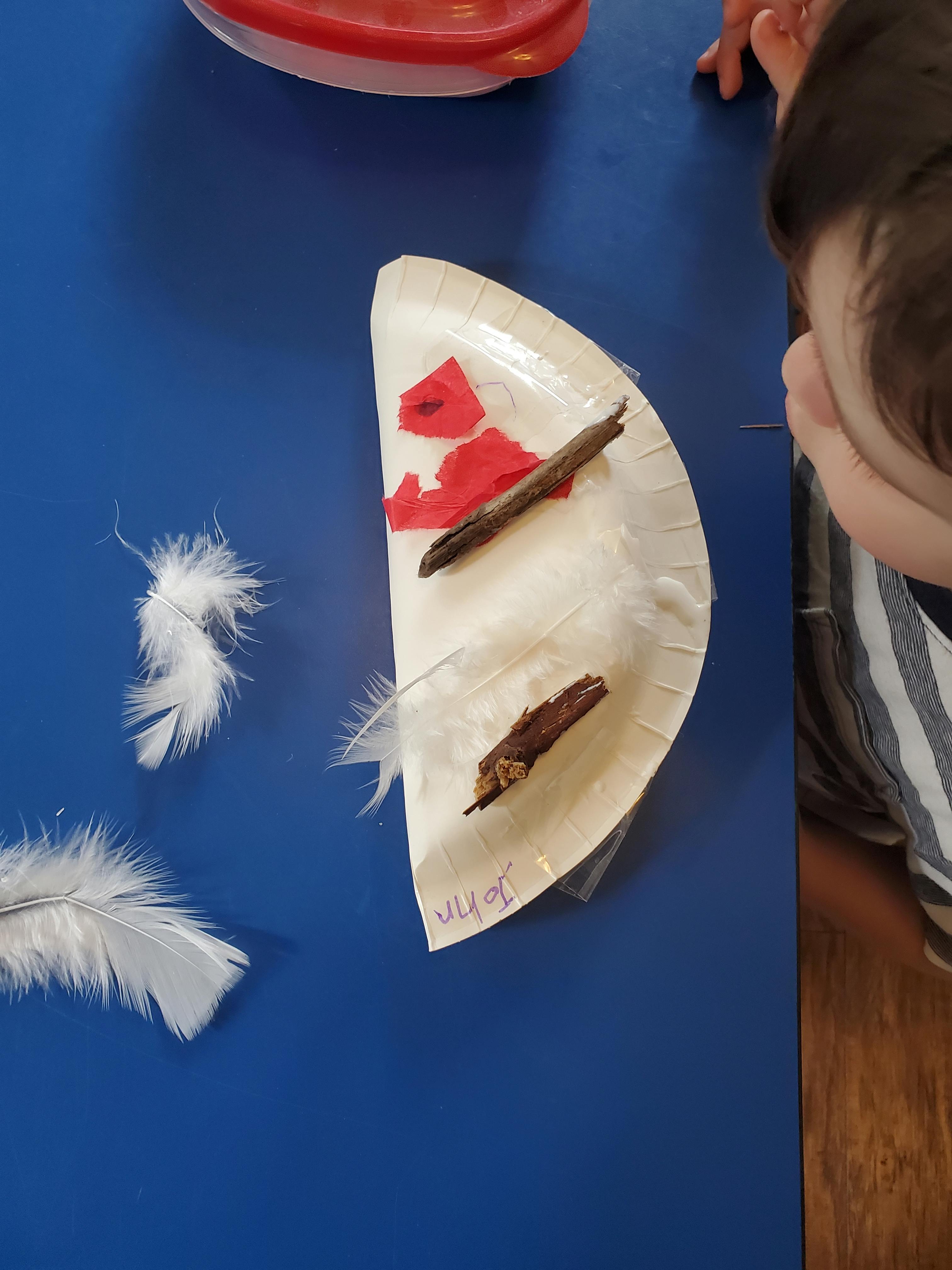 Child looking at a paper plate craft with feathers and sticks