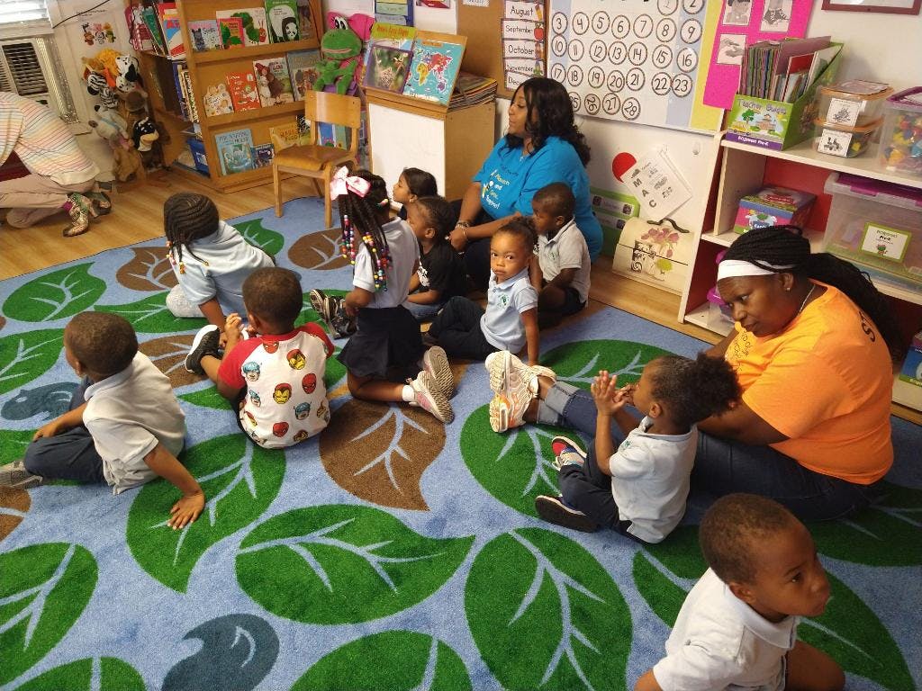 Adults and children sitting on a leaf-patterned rug in a classroom