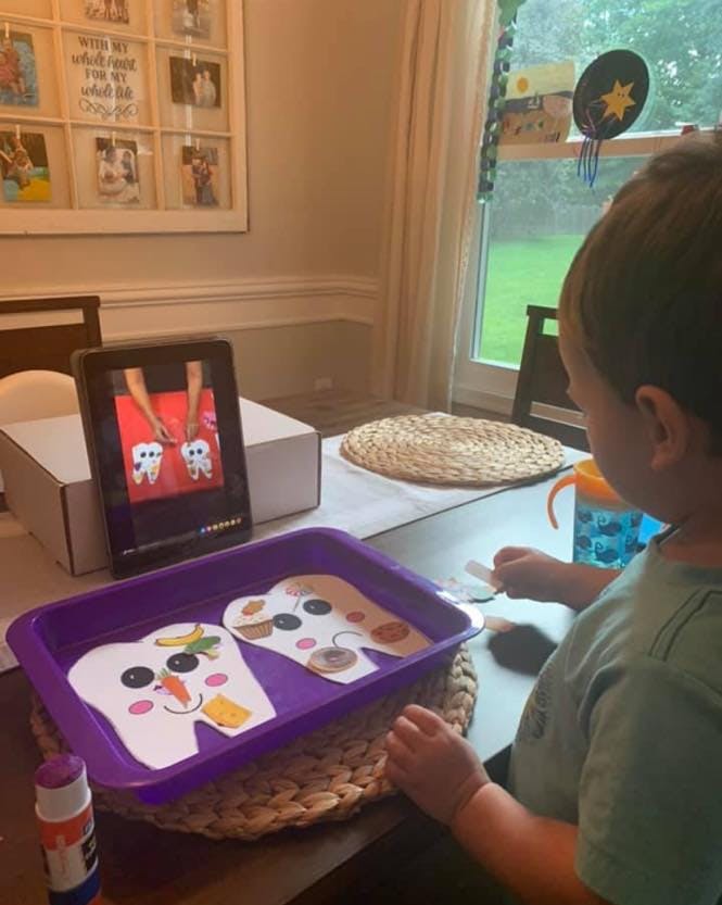 Child playing with tooth-shaped cutouts and watching a tablet