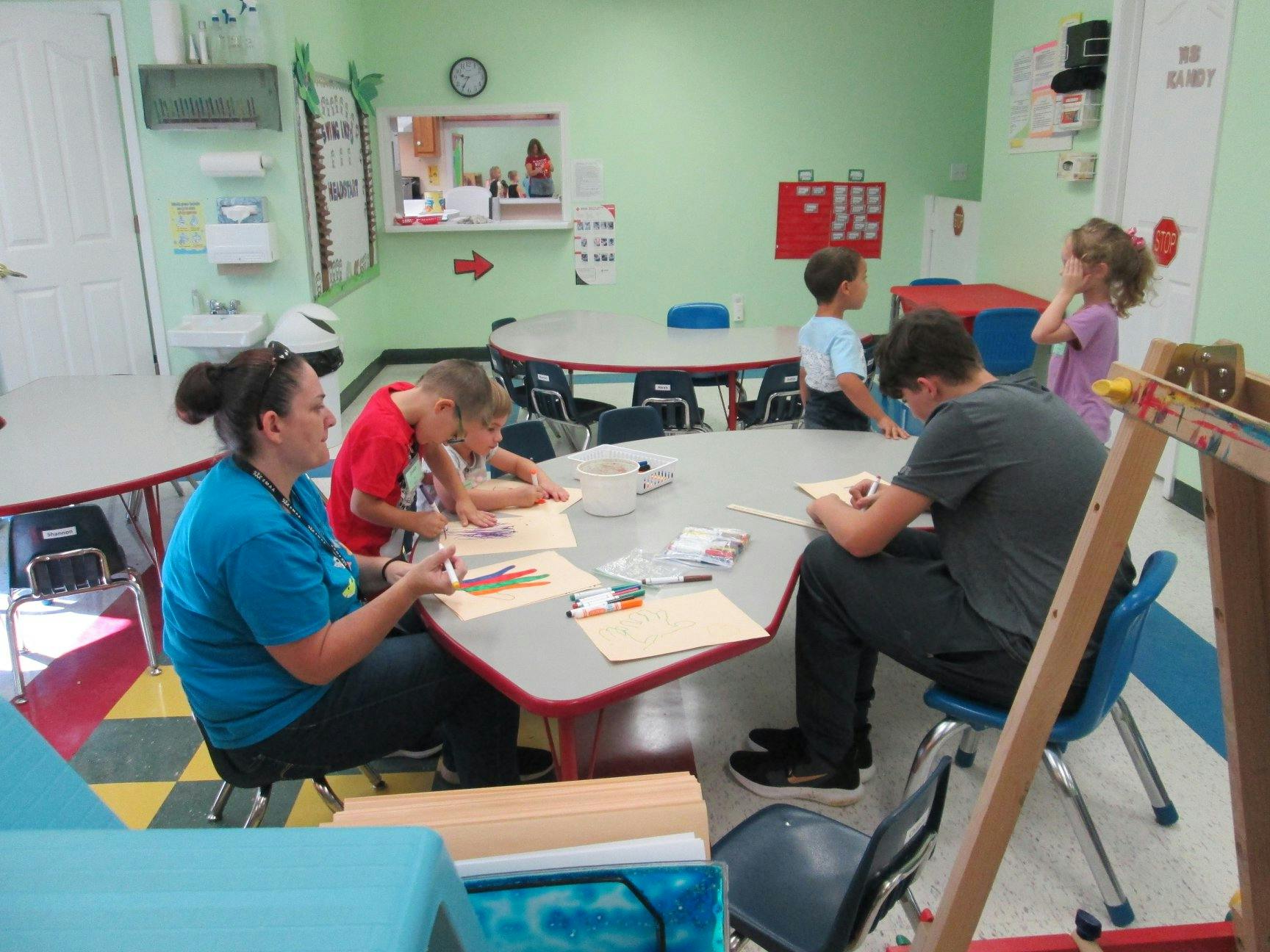 Adults and children working at tables in a classroom