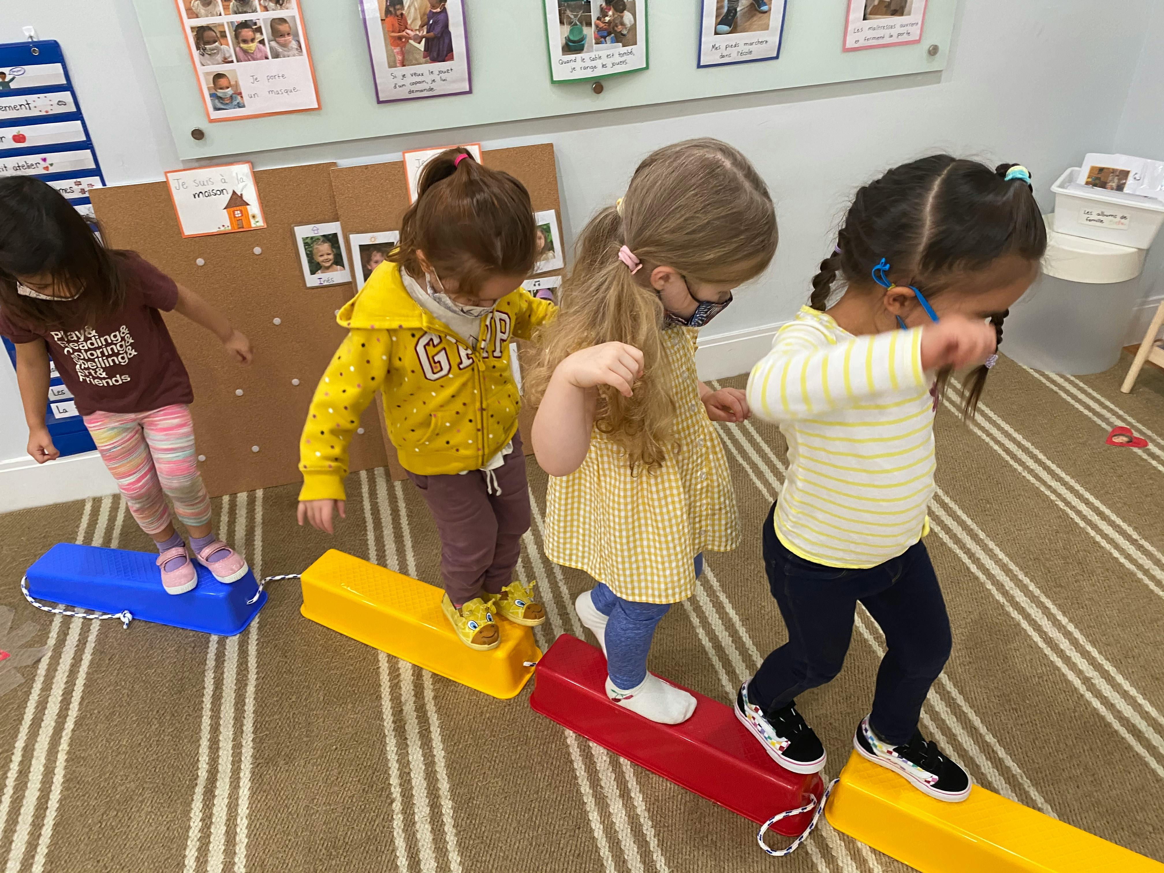 Four children walking on colorful balance beams indoors