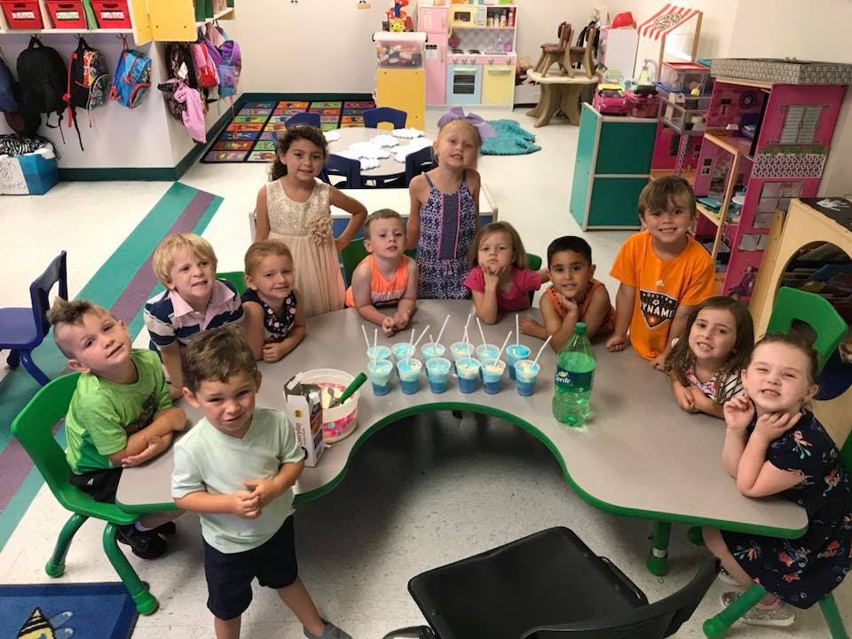 Children gathered around a table with drinks in a classroom