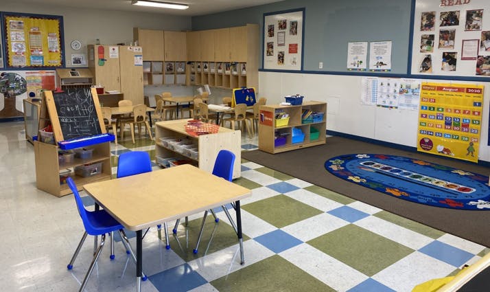 Empty classroom with small tables and chairs, storage units, and a calendar