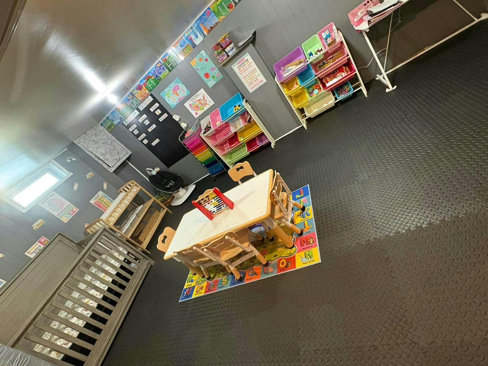 Childcare room with a table, alphabet rug, and storage shelves