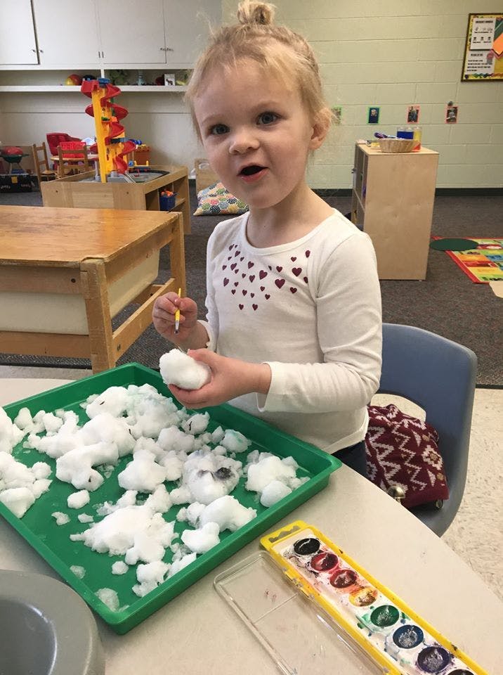 Child holding a snowball over a tray of snow in a classroom