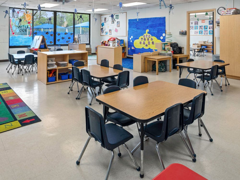 Empty classroom with small tables and chairs, and a colorful rug on the floor