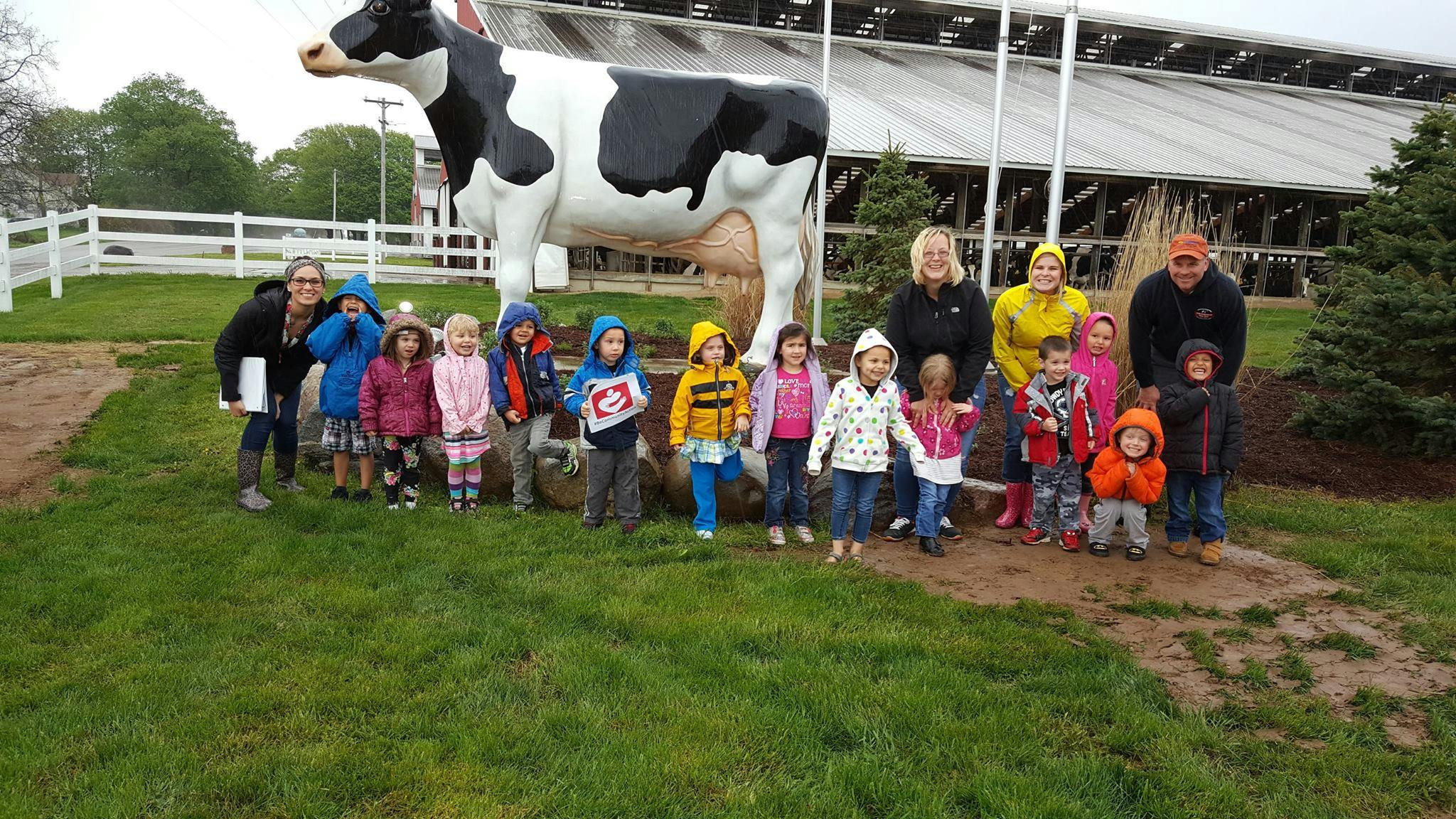 Group of children and adults standing in front of a large cow statue