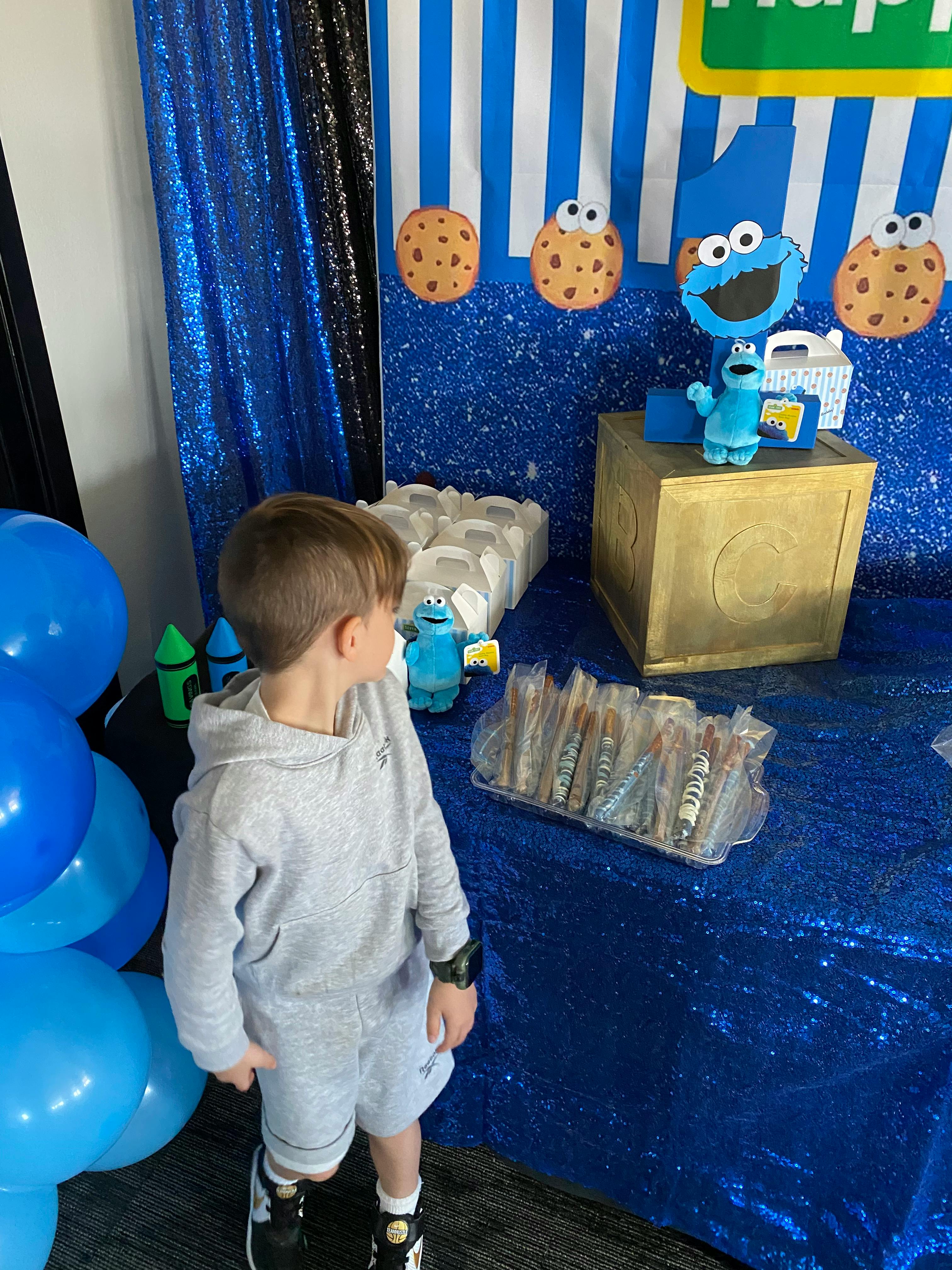 Child standing next to a table with blue decorations and balloons