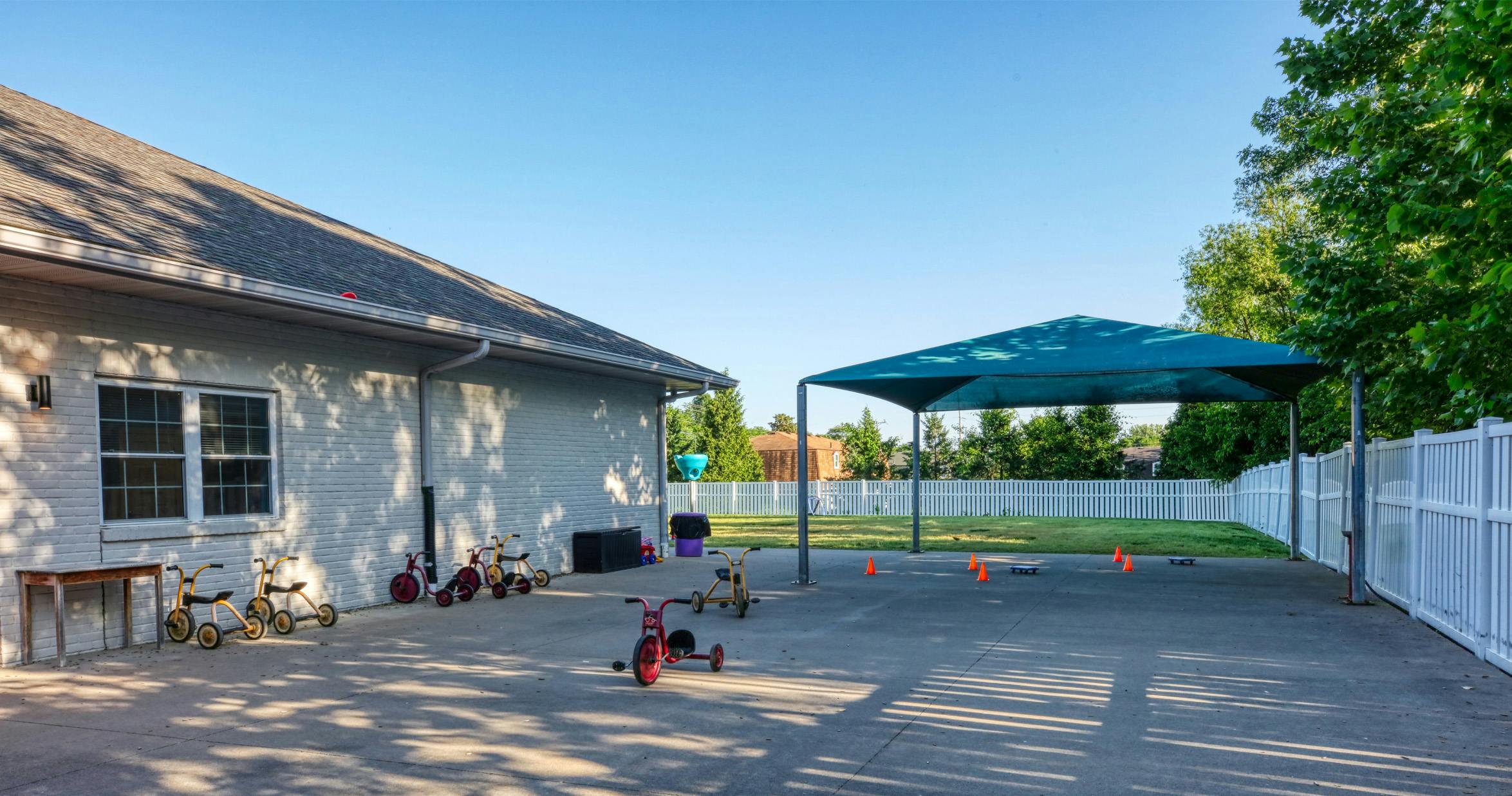 Playground with multiple tricycles on a concrete area, shaded by a blue canopy