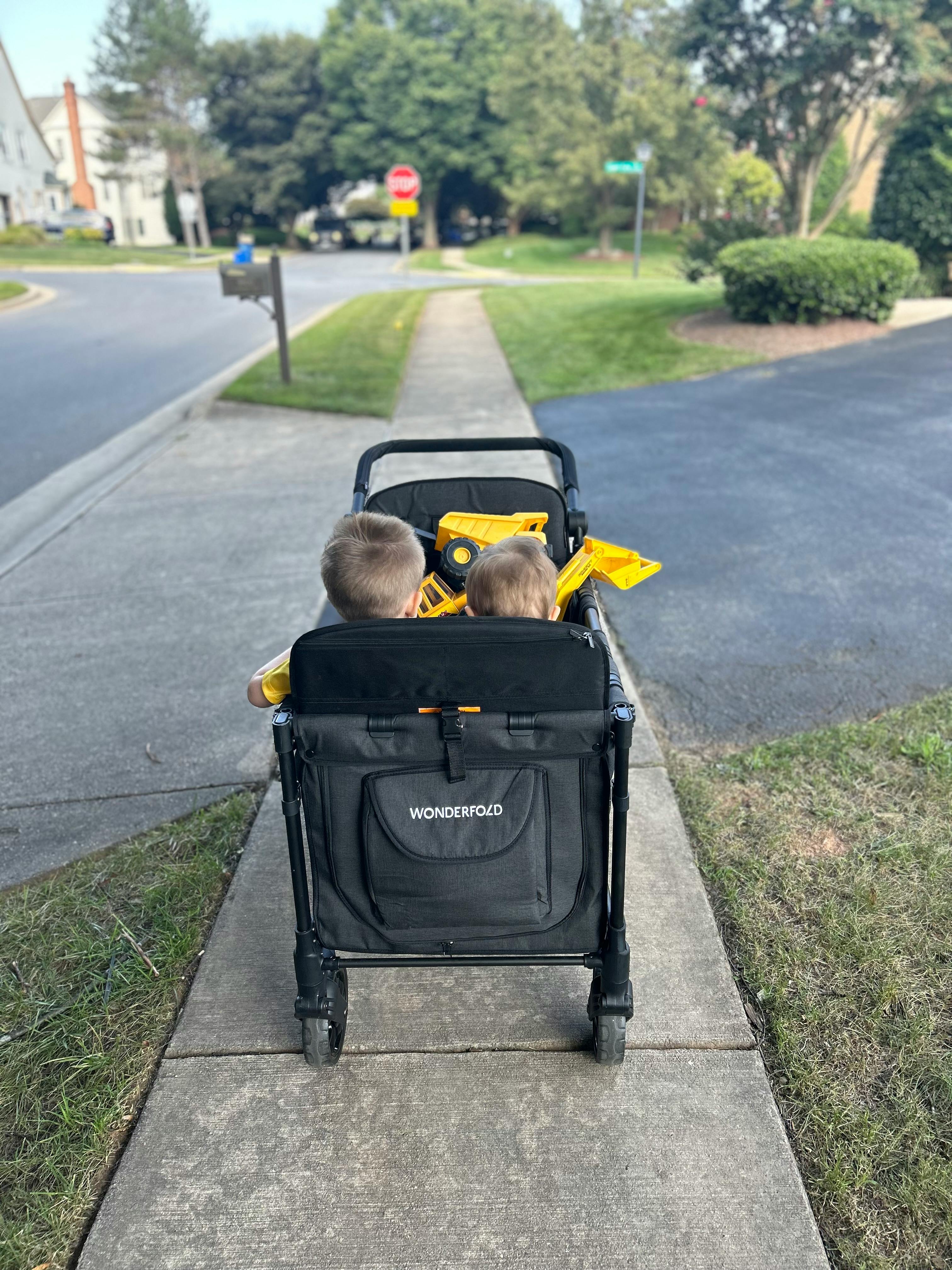 Two children riding in a wagon on a sidewalk