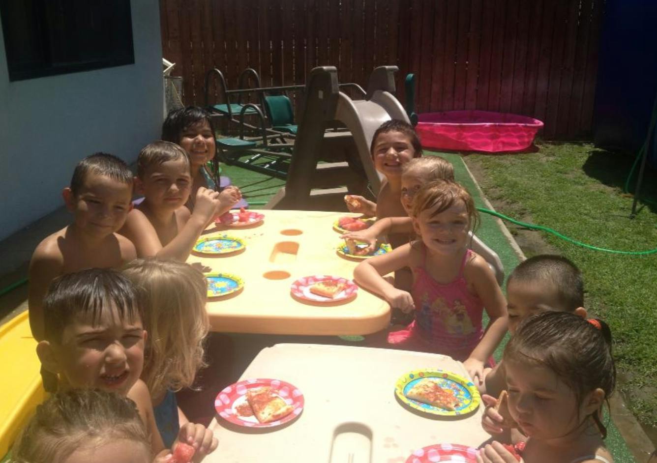 Children sitting at tables with plates of food outdoors