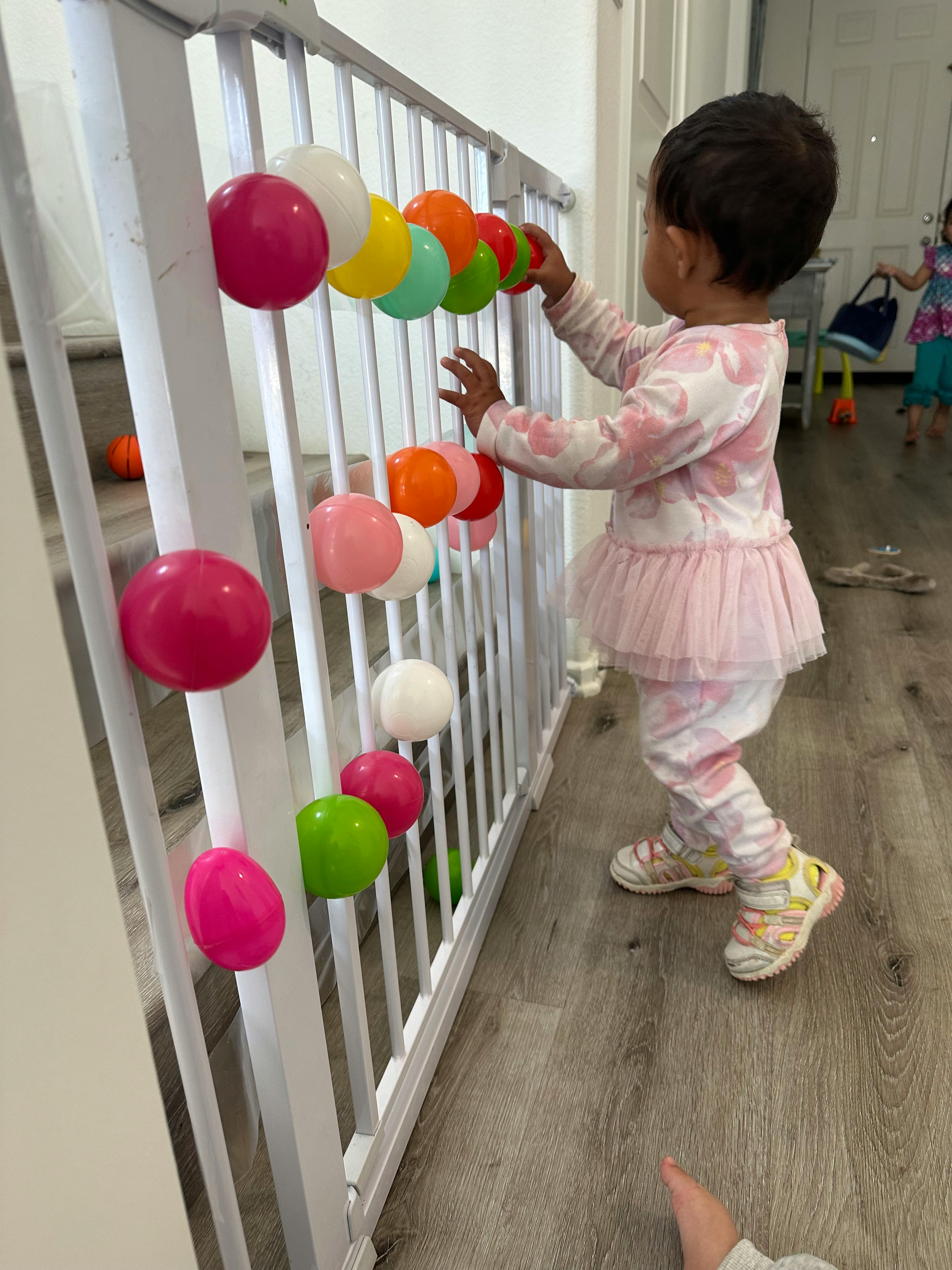 Child playing with colorful balls attached to a white stair railing