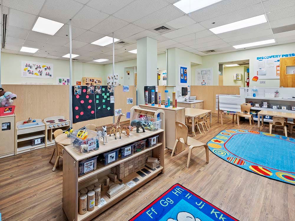Classroom with small wooden tables and chairs, shelves, and rugs