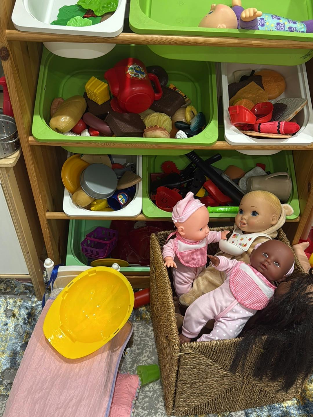 Doll figures in a woven basket next to shelves filled with toy food and items