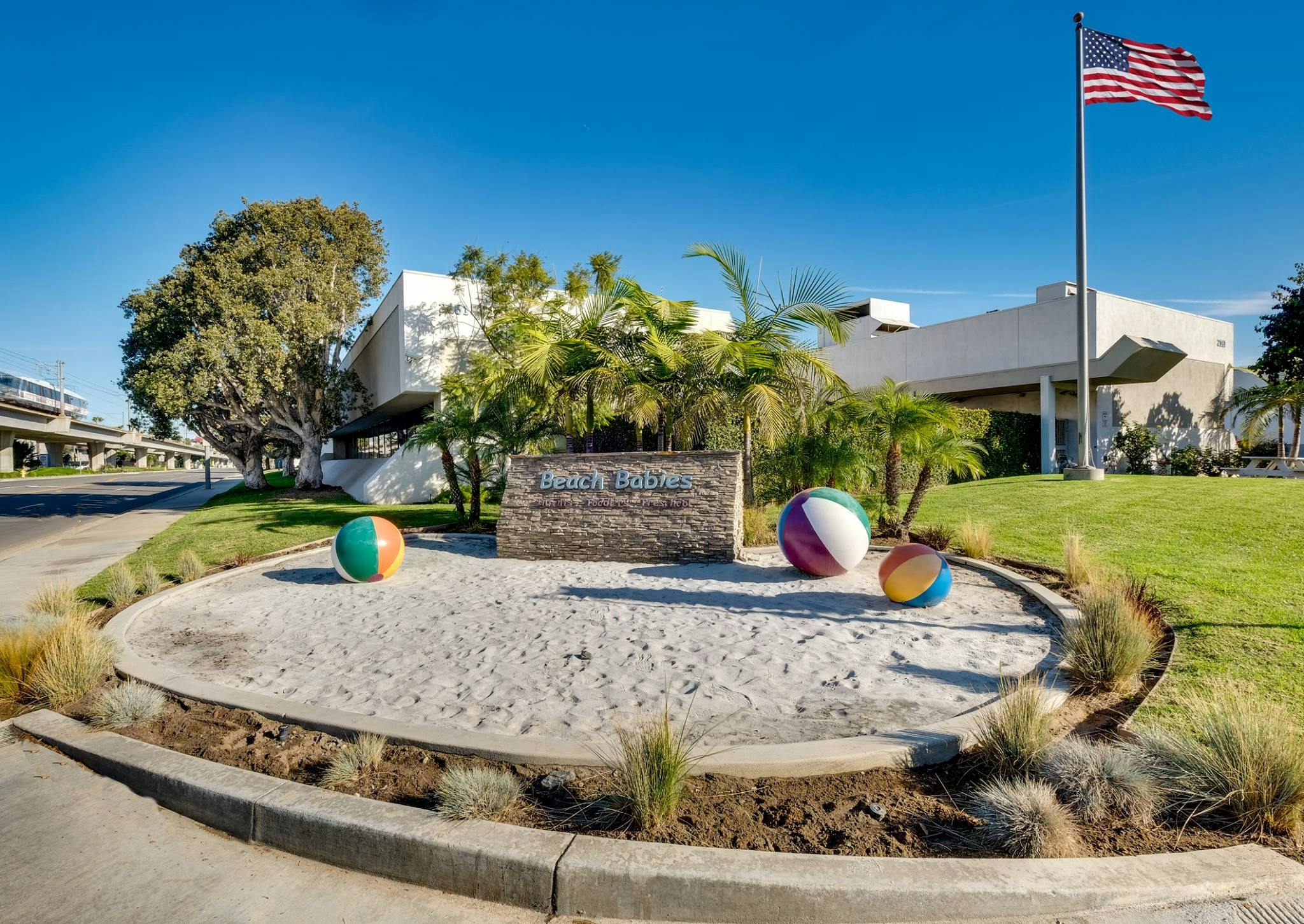 Landscaped area with sand, beach balls, and a sign in front of a building